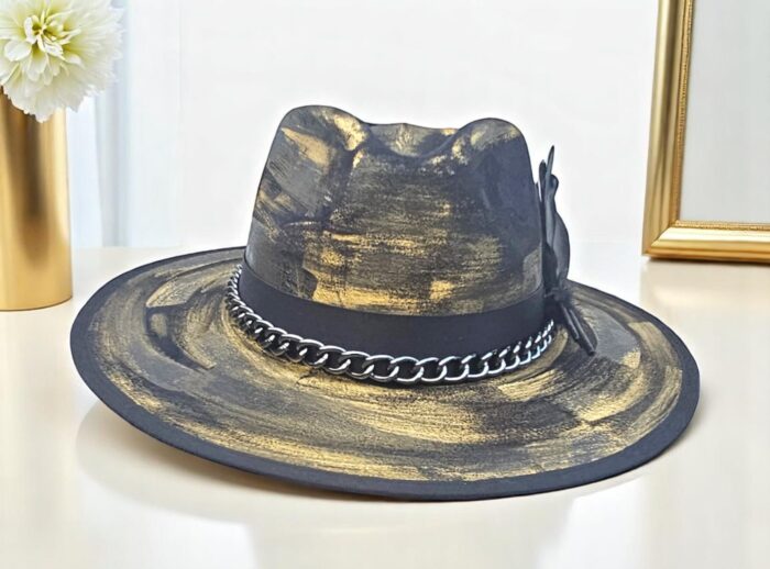 Power. Contrast. Mystery. This hand-painted hat blends deep black with bold golden strokes and a sleek metal chain for an edgy finish. One-of-a-kind, one-size (55–58 cm), crafted for those who turn every appearance into a statement of style.